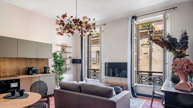 A modern living room with a grey sofa, a dining table with chairs, a coffee machine, and a TV.
