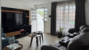 A modern living room with a flat-screen TV, a sofa, a coffee table, and a potted plant.