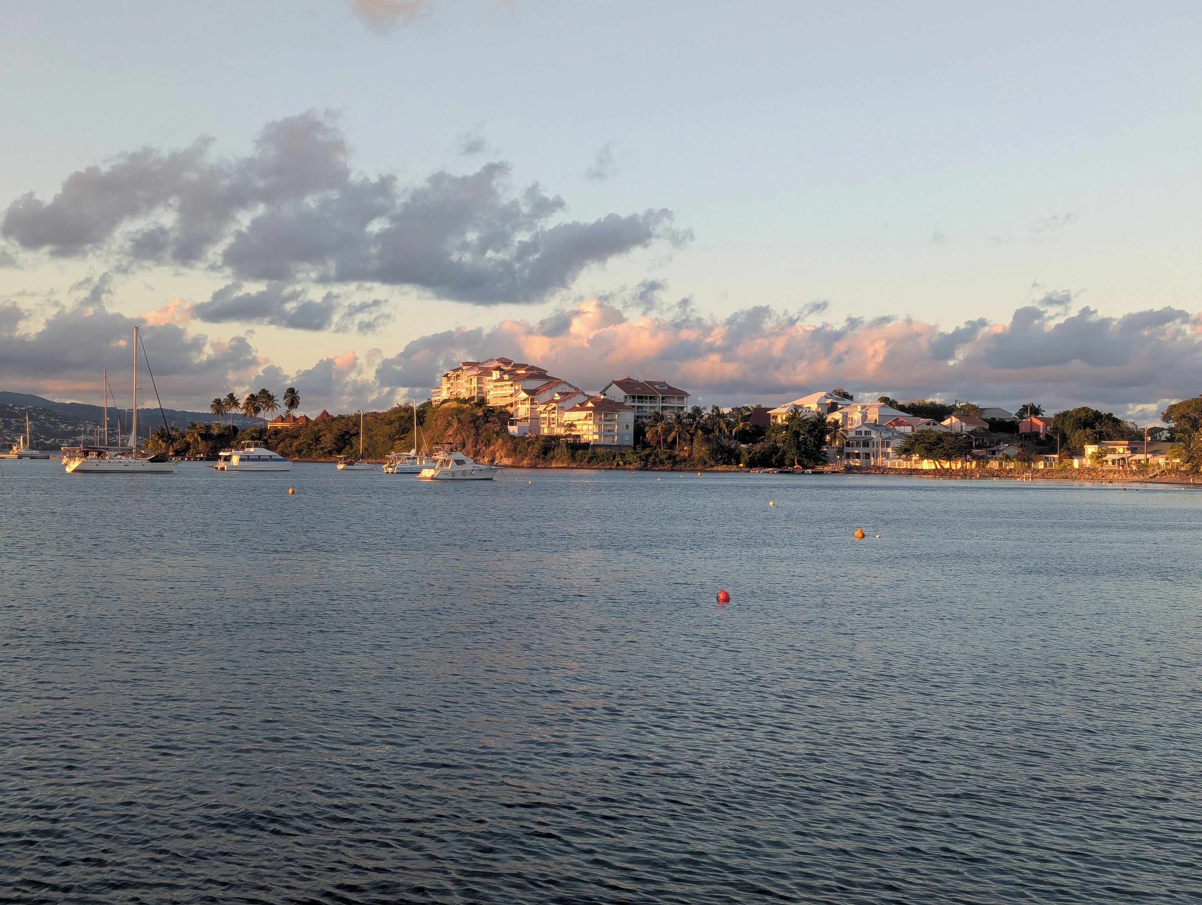 A coastal scene with a large building on a hill, boats on the water, and a clear sky.