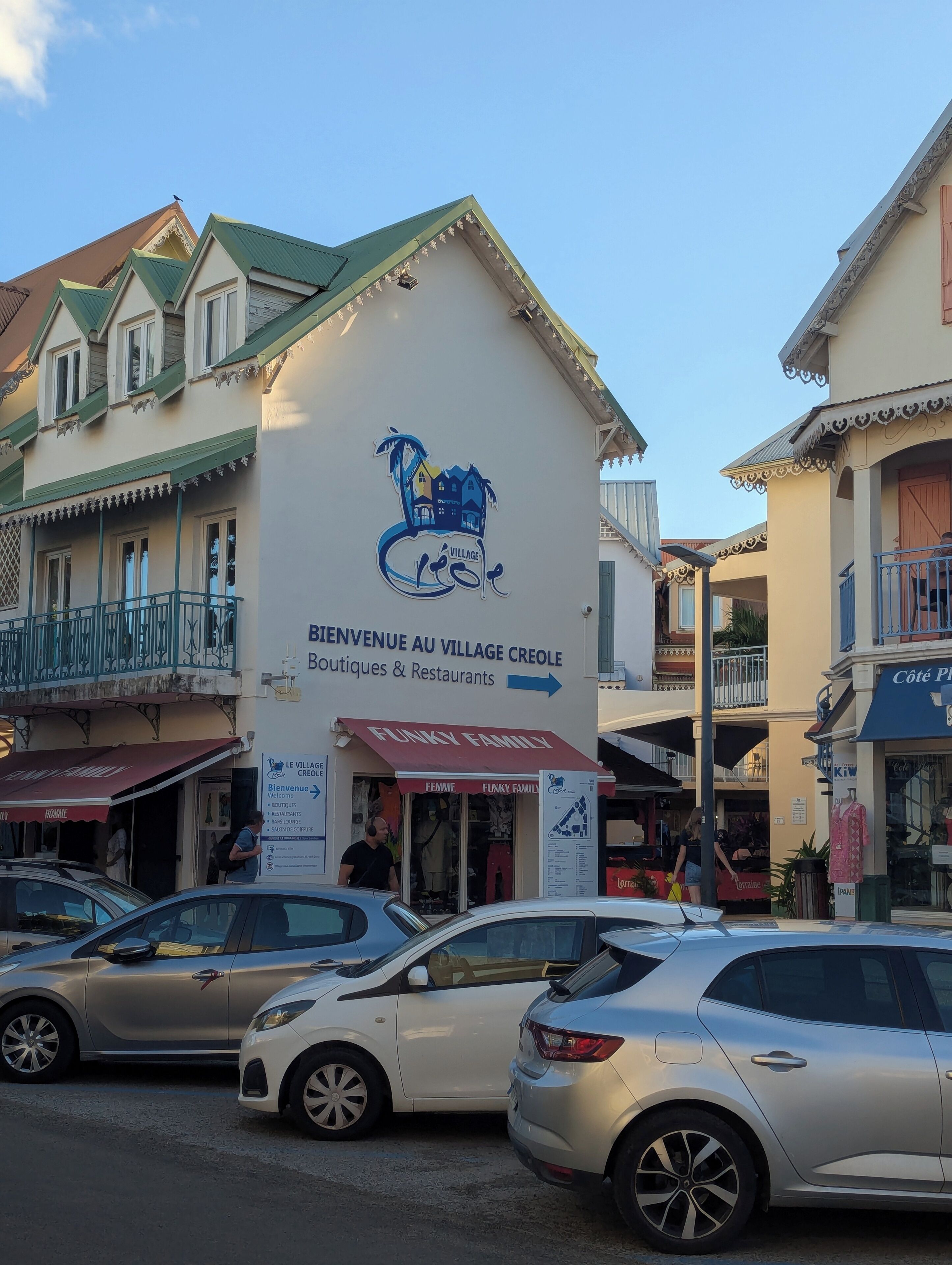 A building with a sign reading 'Bienvenue au Village Creole Boutiques & Restaurants' and a storefront named 'Funky Family.'