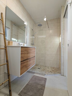 A bathroom with a shower, a wooden vanity, a mirror, and a tiled floor.