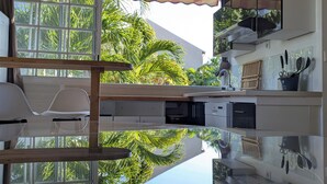 A modern kitchen with a large window, white cabinetry, and a view of palm trees. - Studio Zaboka - Beaches & Marina Ideal for couples, many activities on foot! (Les Trois-Îlets)