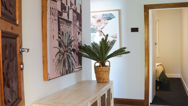 Un couloir avec un banc en bois, une plante en pot et un tableau représentant un paysage urbain accroché au mur.