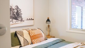 Une chambre à coucher avec un lit, une fenêtre, une lampe et un tableau encadré accroché au mur.