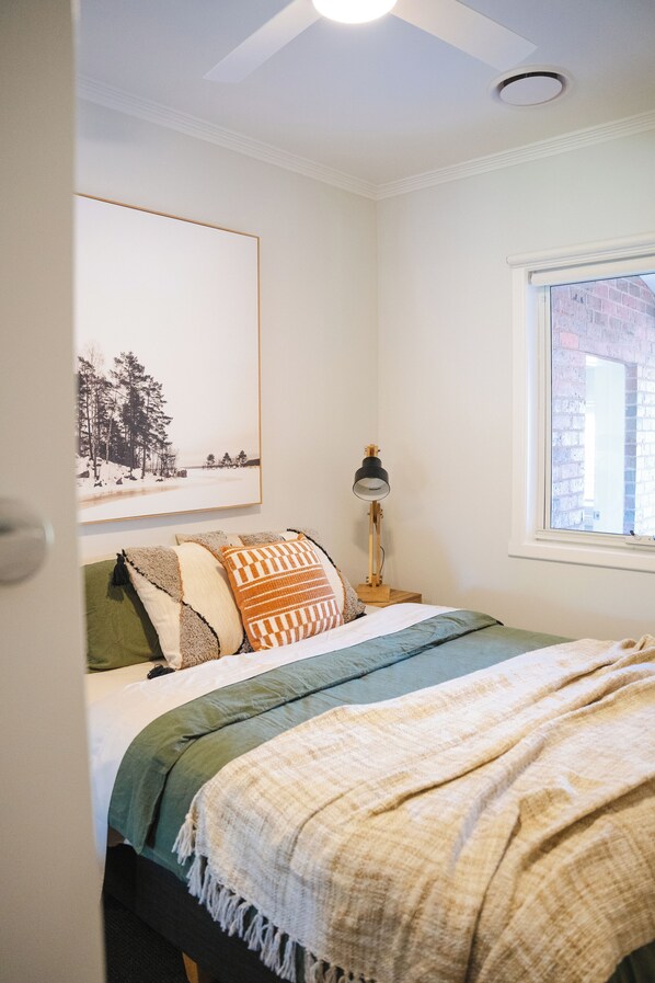 Un dormitorio con cama, ventana, lámpara y un cuadro en la pared.