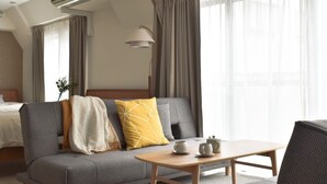 Ein Hotelzimmer mit einer Couch, einem Tisch mit Teekannen, einer Lampe und einem Bett im Hintergrund.