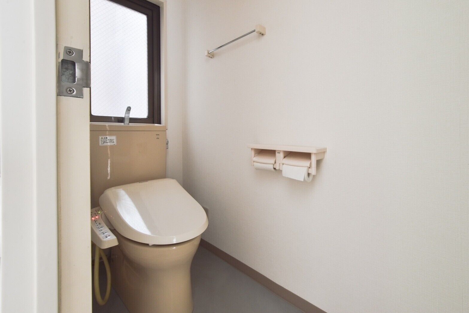 A small, compact bathroom with a toilet, a window, and a wall-mounted toilet paper holder.