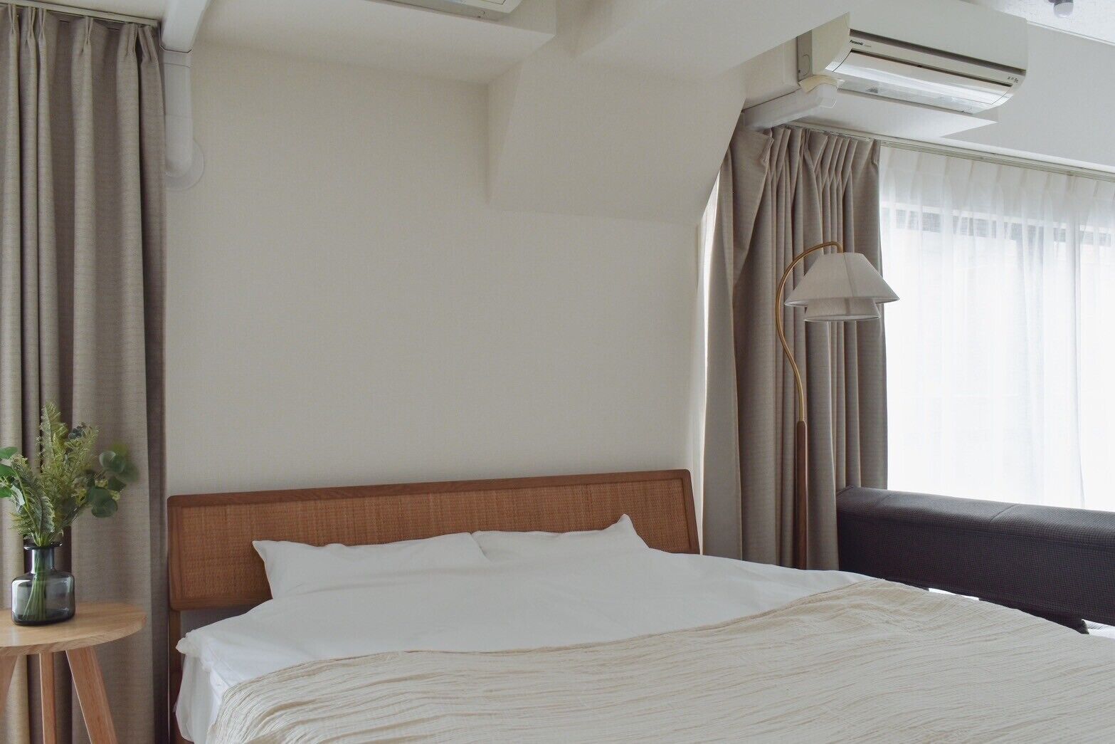 A hotel room with a bed, a bedside table with a vase, a lamp, and a window with curtains.