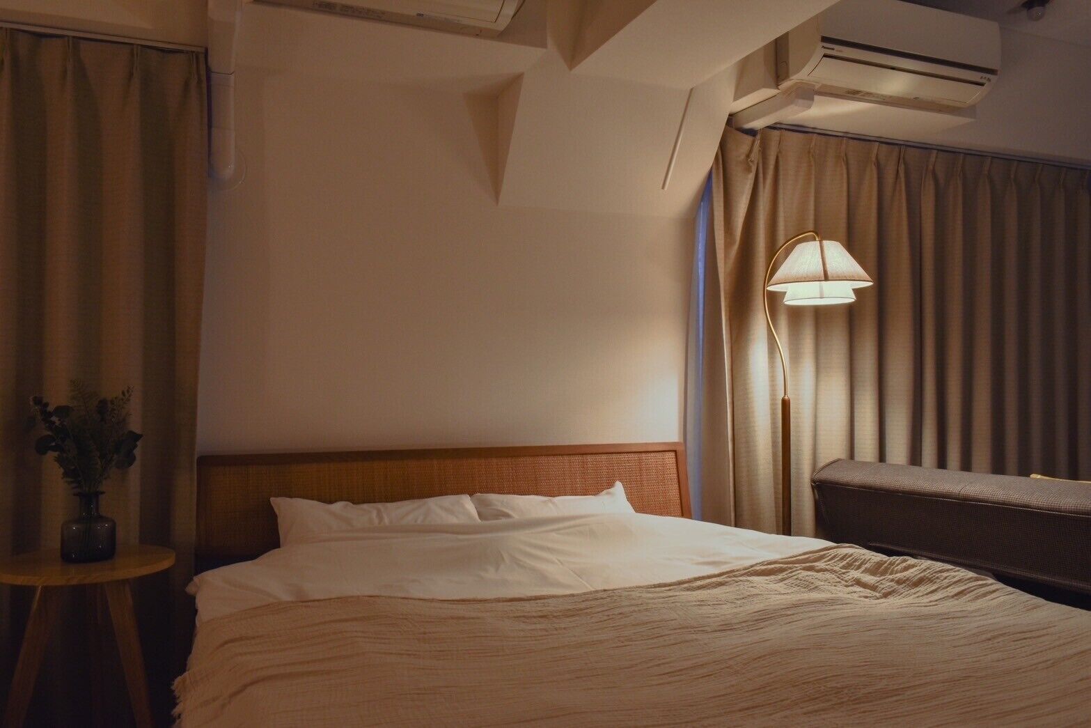 A hotel room with a bed, a bedside table with a vase, a lamp, and a chair.