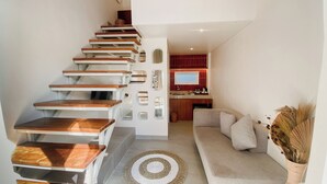 A modern interior with a wooden staircase, a living area with a sofa and a decorative rug, and a kitchen with red tiles and a flat-screen TV. - Escotel Melasti (Ungasan)