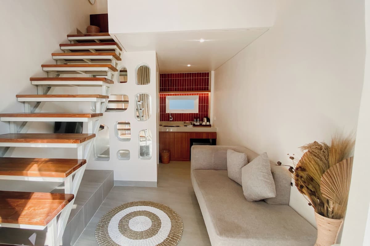 A modern interior with a wooden staircase, a living area with a sofa and a decorative rug, and a kitchen with red tiles and a flat-screen TV.