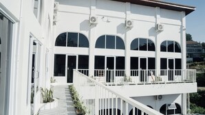 A white building with multiple arched windows, a balcony with railings, and a staircase leading to the entrance. - Escotel Melasti (Ungasan)