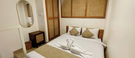 A neatly made bed with a heart-shaped towel arrangement, a bedside table, a mirror, and a traditional woven partition.