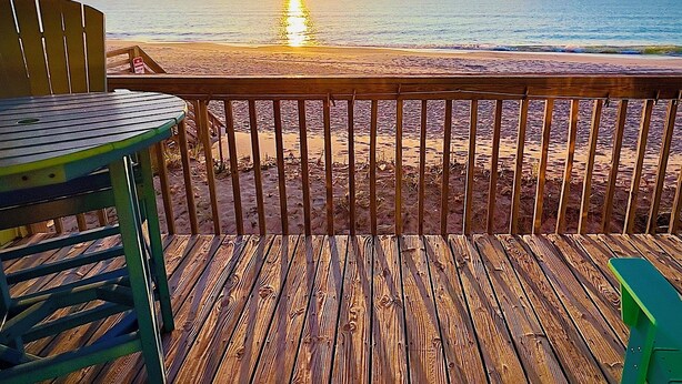 A wooden deck with a table and chairs overlooking a beach at sunset. - The Endless Wave: Oceanfront Condo, Sunrise View, Pool, 1-mile to Dining & Pier (Surf City)