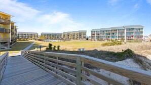 A beachfront hotel with multiple balconies, a wooden boardwalk, and a grassy area. - The Endless Wave: Oceanfront Condo, Sunrise View, Pool, 1-mile to Dining & Pier (Surf City)