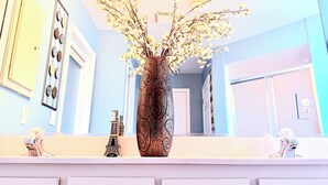 Un baño con un espejo, un florero con flores y una pequeña reproducción de la Torre Eiffel sobre el mostrador.