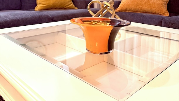 Una sala de estar moderna con una mesa de centro de vidrio, un sofá oscuro con cojines amarillos y un reloj decorativo en la pared.