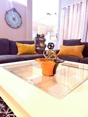 A modern living room with a glass coffee table, a dark sofa with yellow cushions, and a decorative clock on the wall. - Peaceful, Relaxing & Quiet Home With A Private Fenced Yard In Ocala FL (Ocala)