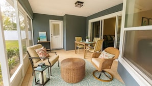 Una habitación acogedora con una mesa de comedor, sillas y un reposapiés de mimbre.