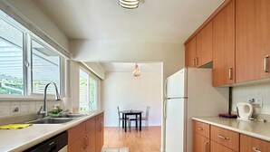 A compact kitchen with wooden cabinets, a built-in dishwasher, a refrigerator, and a window providing natural light.