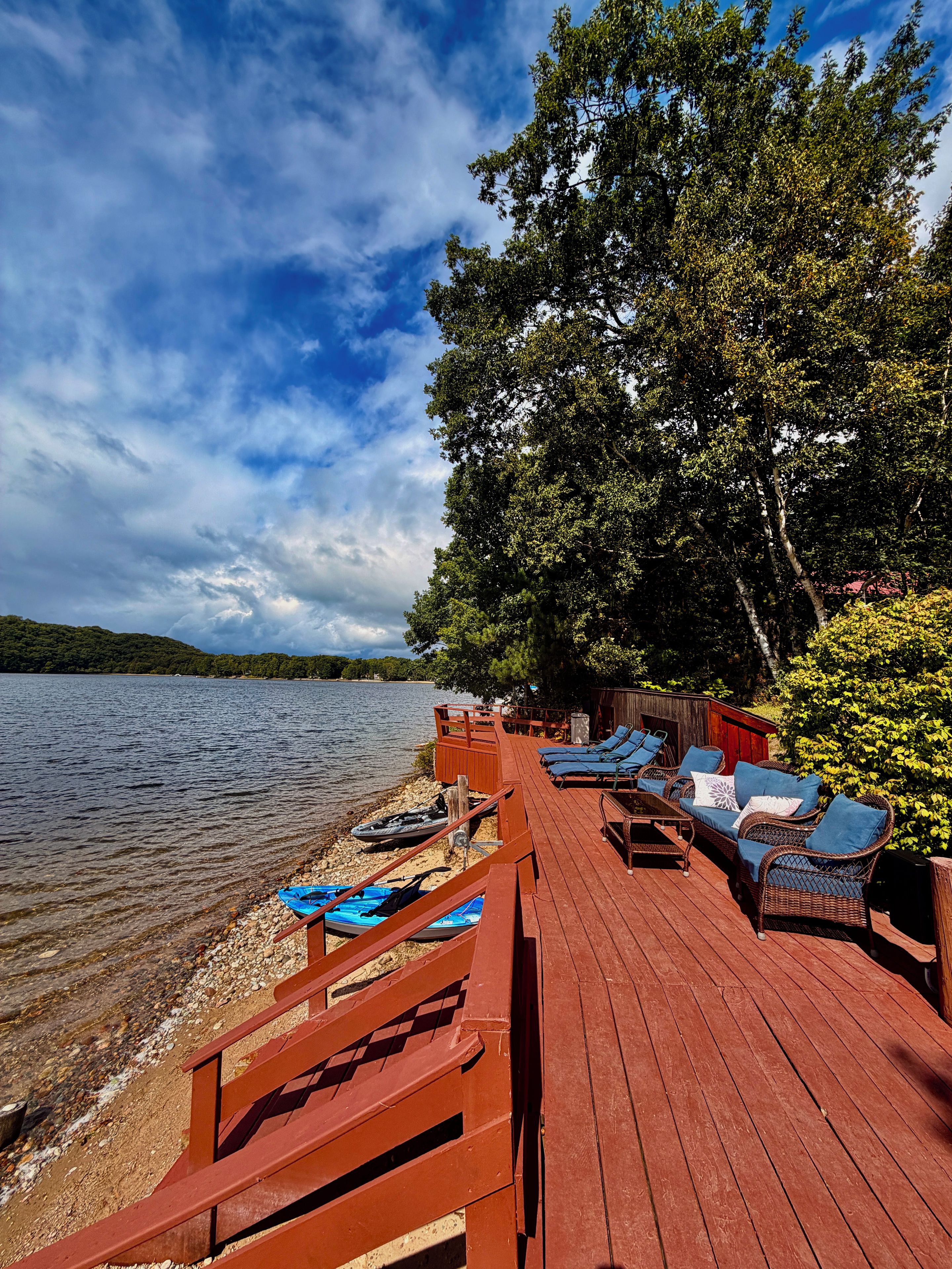 A wooden deck with lounge chairs and a table, overlooking a lake with boats and a dock.