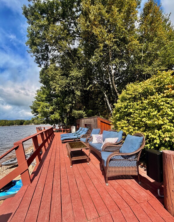 A wooden deck with lounge chairs and a small building, overlooking a body of water.