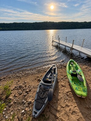 A kayak and a canoe on a pebbly shore with a wooden dock extending into calm water. - Lakefront Retreat - Dock, Beach + Bunkhouse (Brimley)