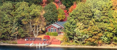 Un chalet au bord du lac, doté d’un quai, entouré d’une forêt dense aux couleurs automnales.