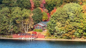 A lakeside cabin with a dock, surrounded by dense forest with autumn foliage.