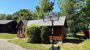 A basketball hoop installed on a wooden building with a gravel driveway and surrounding greenery. - Fall Lakefront Escape on Monocle Lake with Private Dock + Bunkhouse (Brimley)