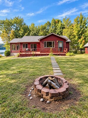 A red cabin with a deck, a fire pit, and a lake view. - Lakefront Retreat - Dock, Beach + Bunkhouse (Brimley)