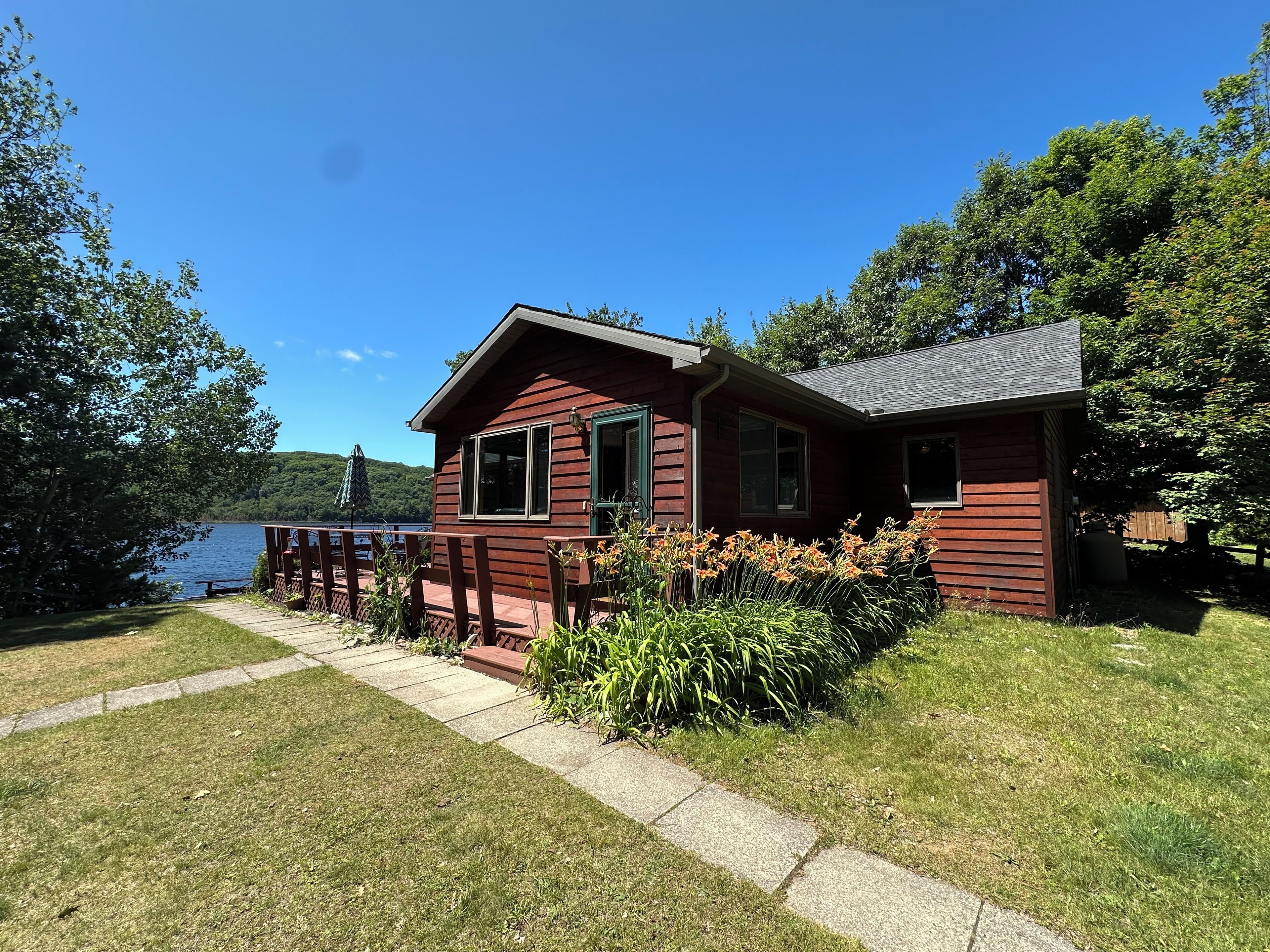 A cabin with a deck overlooking a lake, surrounded by greenery.