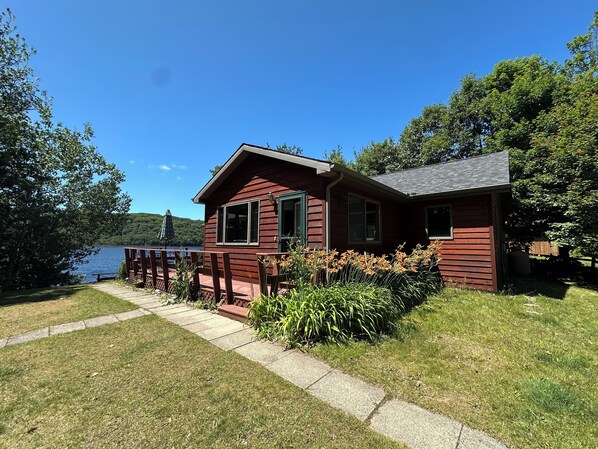 A cabin with a deck overlooking a lake, surrounded by greenery.