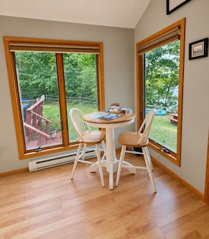 A room with a round table and two chairs, large windows, and a view of a backyard.
