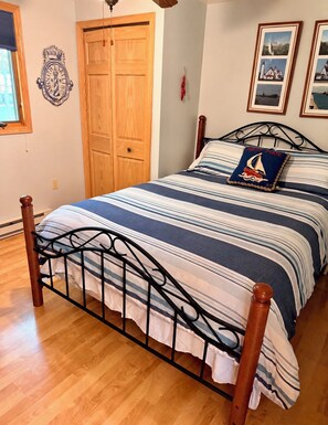 A bedroom with a bed, wooden floor, a door, and a wall-mounted coat rack.