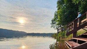 Ein ruhiger See mit einem hölzernen Steg, der sich ins Wasser erstreckt, umgeben von Bäumen und einem klaren Himmel.