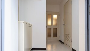 A narrow hallway with a white refrigerator on the left, a door with frosted glass panels in the center, and a door with a vent on the right. - PrinetzShinjuku4F (Tokyo)