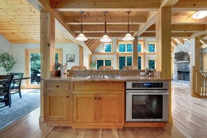 Une cuisine en bois dotée d’un îlot central, d’un four encastré et de luminaires suspendus.