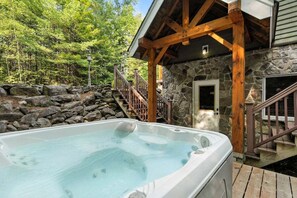 Un bain à remous situé dans un cadre naturel, avec un bâtiment en pierre et une terrasse en bois.