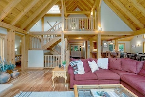 Un vaste espace de vie de style loft, doté d’un haut plafond, d’un escalier en bois, d’un canapé d’angle rouge et d’un coin repas.