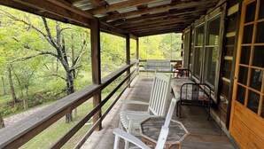 A covered outdoor seating area with wooden benches and a railing, overlooking a forested area.
