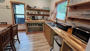 A kitchen with wooden cabinets, a sink, a coffee maker, and shelves with glassware.