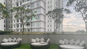 Una terraza en la azotea con tres sofás redondos de mimbre y cojines, rodeada de césped artificial verde.