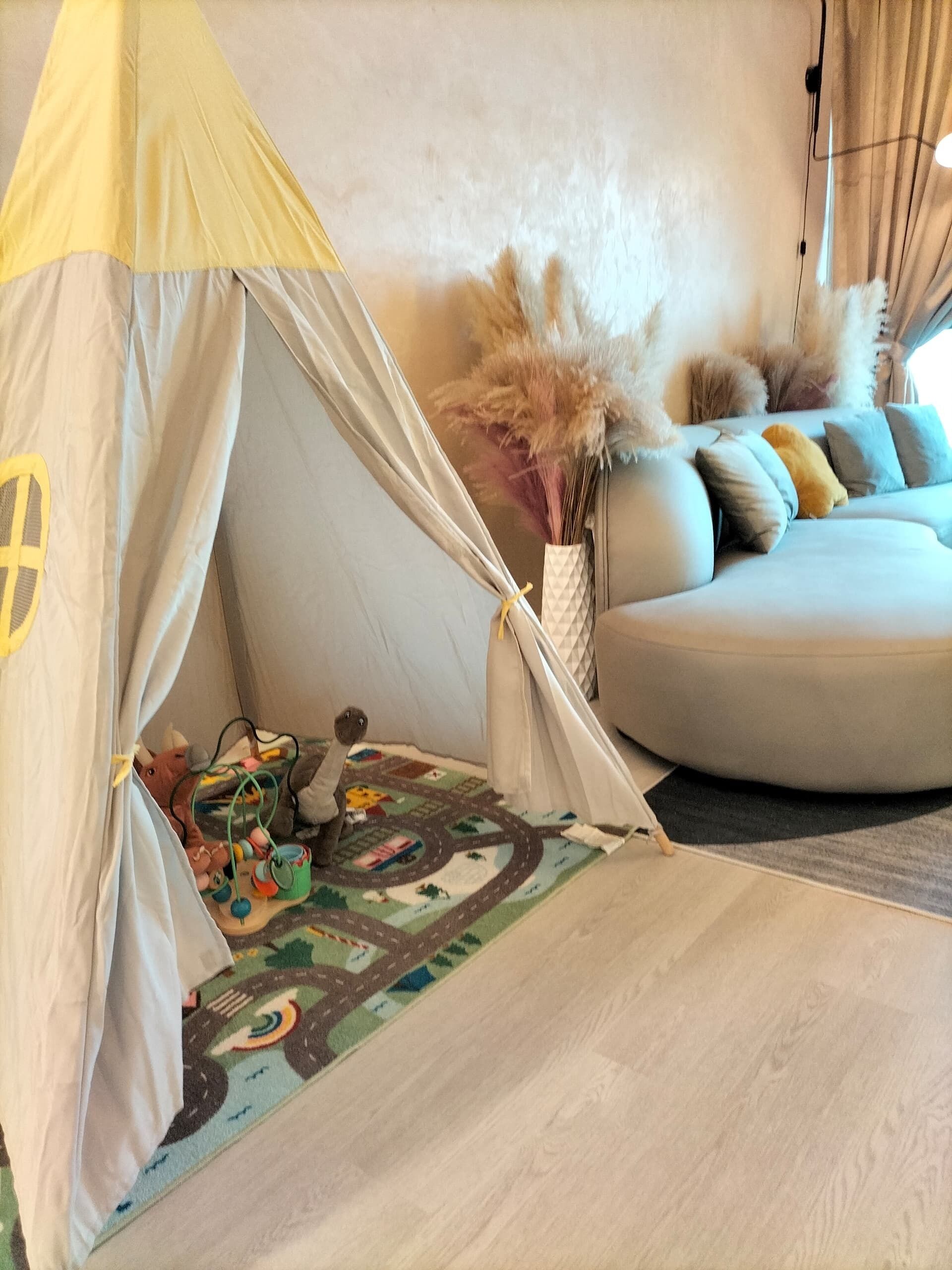 Ein gemütliches Zimmer mit einer zeltartigen Konstruktion, einer Couch und einer bunten Spielmatte.