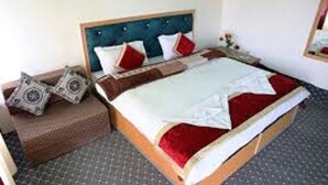 Un lit bien fait, avec une tête de lit en bois, une couvre-lit rouge et blanche et deux coussins décoratifs.