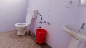 Une petite salle de bain avec des toilettes, un lavabo et un seau rouge.