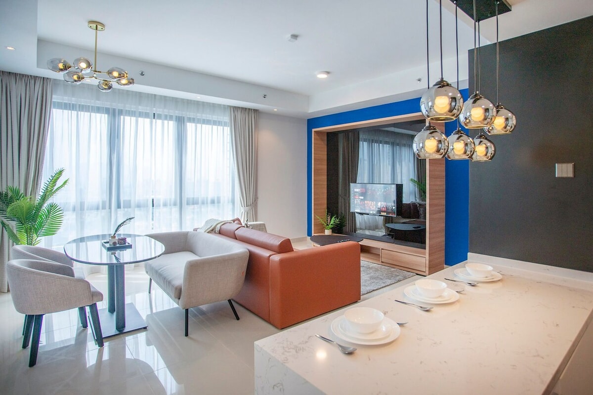 Una sala moderna con un sofá, sillones, una mesa de centro de cristal y un comedor con platos y cubiertos.
