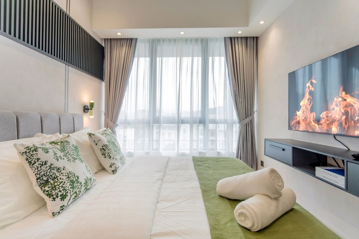 Una habitación de hotel moderna con una cama grande, un televisor de pantalla plana y vistas a la ciudad a través de amplios ventanales.