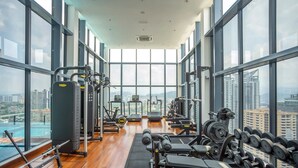 Ein Fitnessstudio mit verschiedenen Trainingsgeräten, großen Fenstern und Blick auf die Stadt.