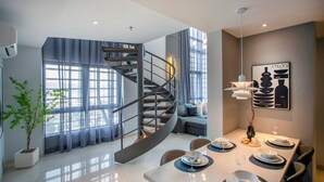 Ein modernes Interieur mit einer Wendeltreppe, einem Essbereich mit Tisch für zwei Personen und einem großen Fenster mit Vorhängen.